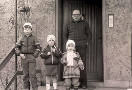 Dzieci i ich dziadek stojący przed budynkiem.